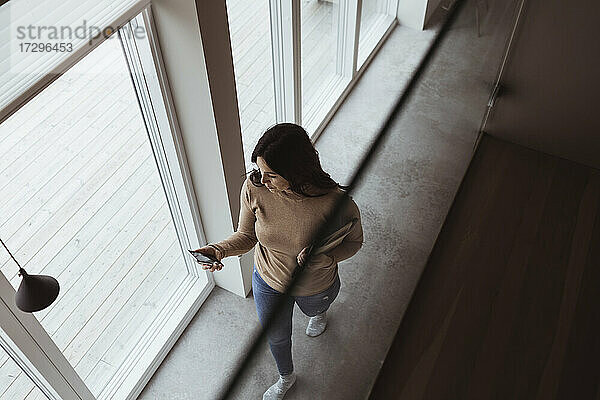 Hohe Winkel Ansicht der Geschäftsfrau mit Smartphone während des Gehens zu Hause