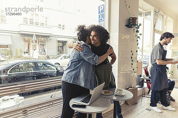 Männliche und weibliche Freunde umarmen einander im Café