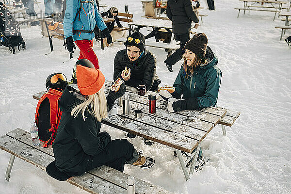 Männliche und weibliche Freunde reden beim Essen Hot Dog im Skigebiet im Winter