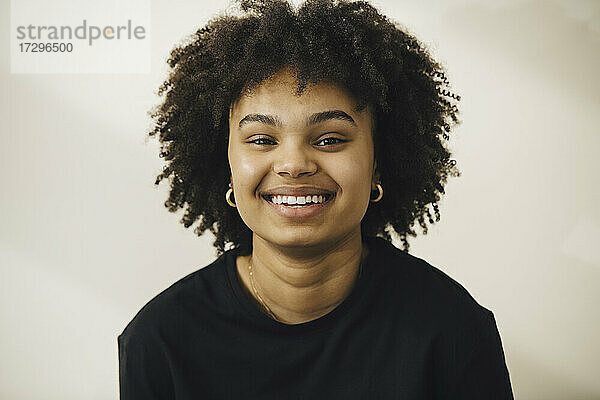 Lächelnde junge Frau mit lockigem Haar gegen beige Hintergrund