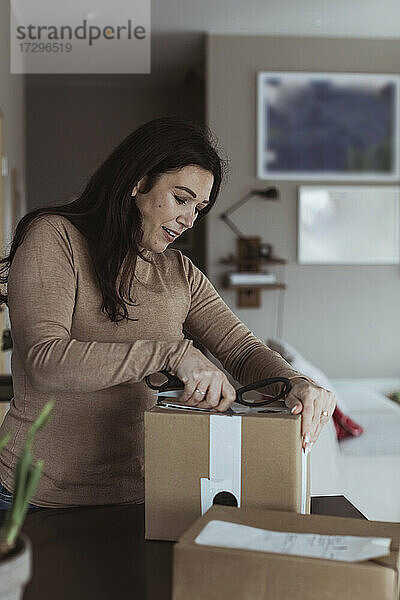 Mid erwachsene Frau Auspacken Box mit Schere zu Hause