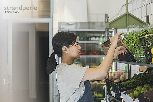 Asiatische Unternehmerin arrangiert Gemüse auf einem Regal im Laden