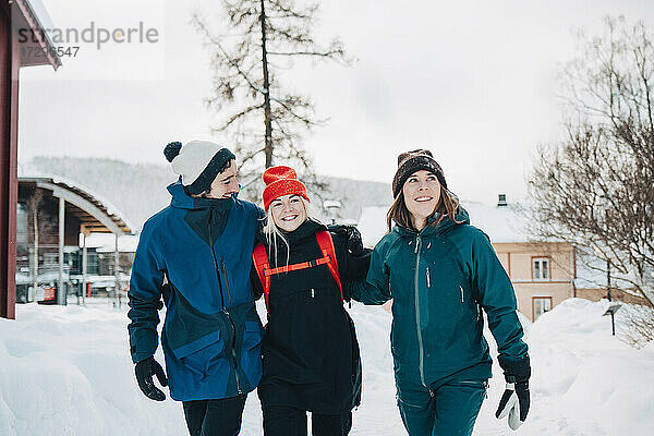 Fröhliche männliche und weibliche Freunde zu Fuß mit Arm um im Skigebiet