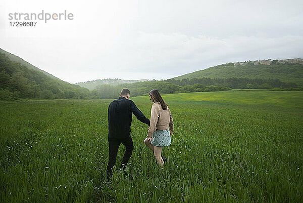 Rückansicht eines jungen Paares  das in einem Weizenfeld im Regen spazieren geht