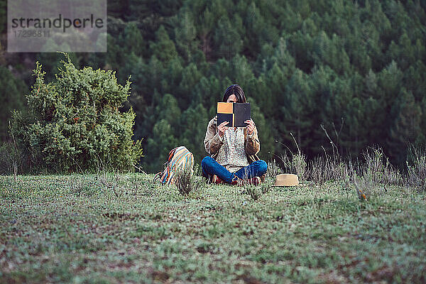 Frau in den Bergen liest ein Buch auf einer Wiese.