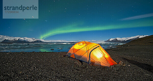 beleuchtetes Zelt in der Arktis mit Nordlichtern am Himmel