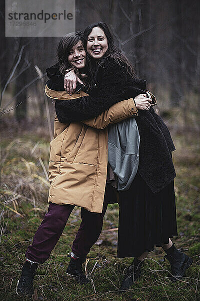 zwei glückliche frauen lächeln und umarmen sich in wintermänteln im deutschen wald