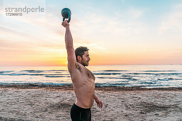 muskulöser Mann beim funktionellen Training mit der Kettlebell am Strand von