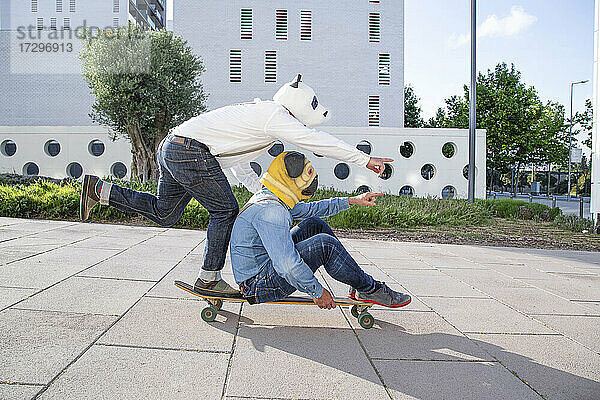 Zwei Männer mit Tiermaske auf Longboard im Park