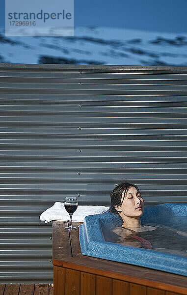 Frau entspannt im Whirlpool vor einem Chalet in Island