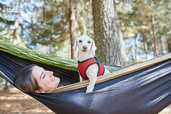 Porträt einer Frau  die sich in einer blauen Hängematte entspannt  mit ihrem Hund im Vordergrund