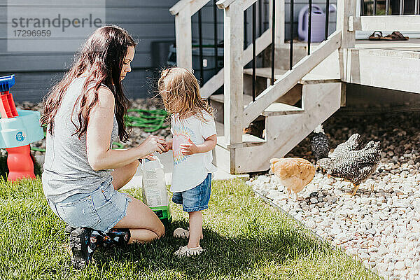 Mutter und Tochter füttern an einem sonnigen Tag Hühner in ihrem Hinterhof