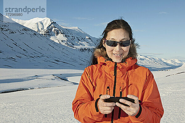 Frau  die in den Bergen von Nordisland eine SMS auf ihrem Smartphone schreibt