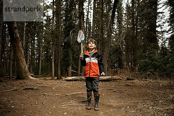 Junge hält Fischernetz im Wald und trägt eine rote Jacke