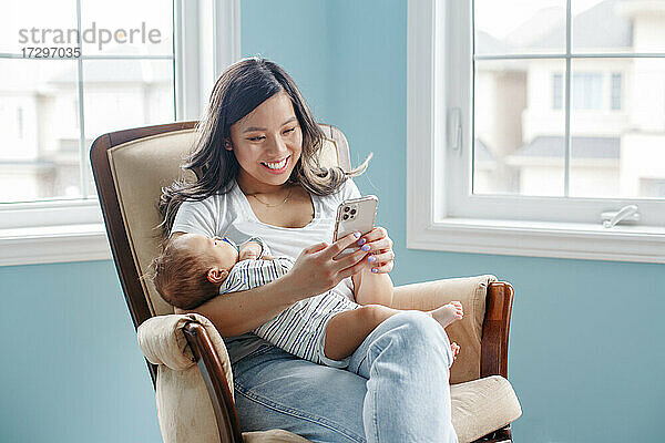 Asiatische Mutter hält neugeborenes Kind Baby Sohn und Chat auf Smartphone