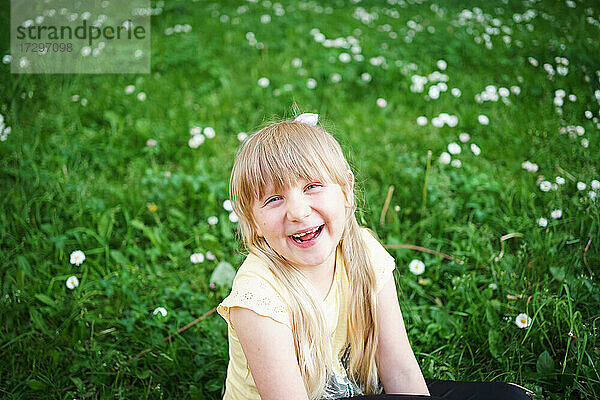 blondes Mädchen lacht auf dem Feld mit Gänseblümchen