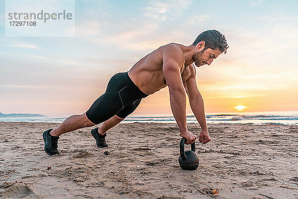 muskulöser Mann beim Core-Training am Strand bei Sonnenaufgang