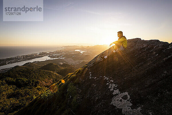 Mann sitzt auf felsigen Bergkante mit schönen Sonnenuntergang Landschaft