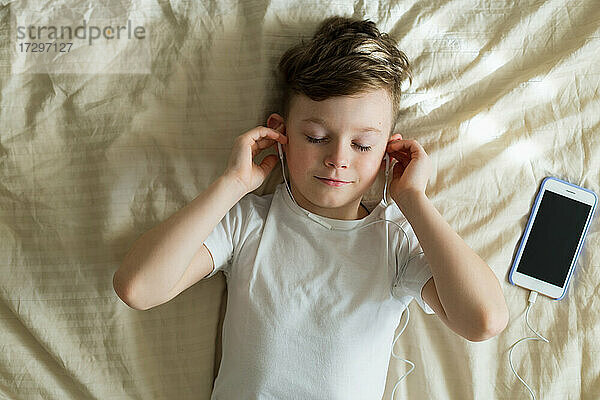 Junge hört Musik mit Kopfhörern auf dem Bett