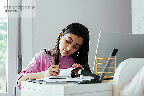 Konzentrierter Teenager beim Lernen am Schreibtisch im eigenen Zimmer