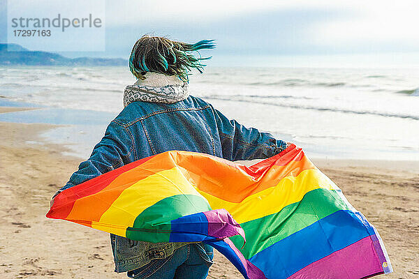 Frau läuft mit bunter LGBT-Flagge  die am Strand weht