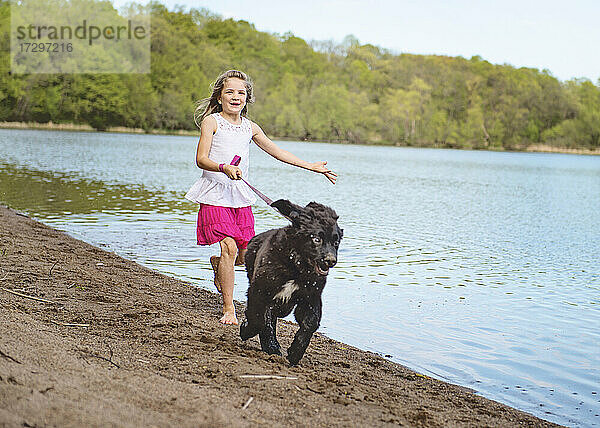 Kleines Mädchen läuft am Strand mit schwarzem Hund