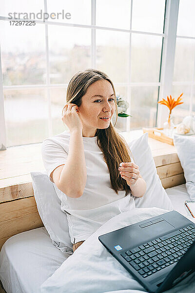 Mädchen arbeitet an einem Laptop und hört Musik im Bett