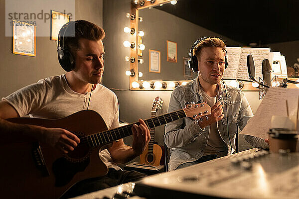 Männlicher Sänger liest Songtexte  während ein Freund im Aufnahmestudio Gitarre spielt