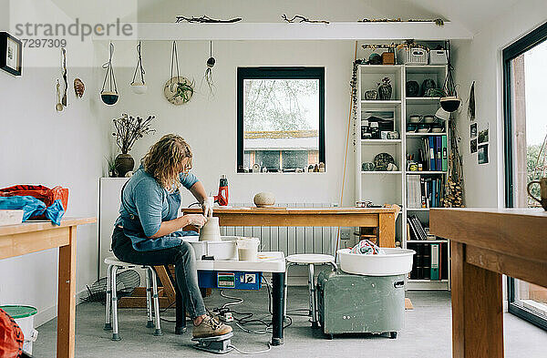 Frau beim Drehen von Ton auf einer Töpferscheibe in ihrem Heimstudio im Vereinigten Königreich