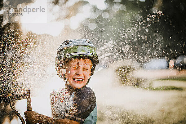 Junger Junge spielt draußen im Sprinkler Wasser spritzen und lachen
