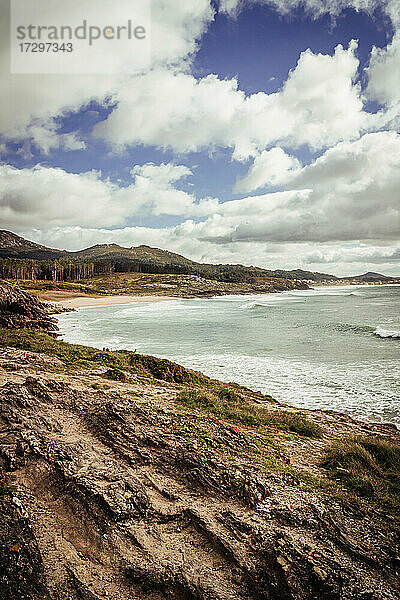 Blick auf eine Klippe mit Strand und Bergen unter blauem Himmel mit Wolken