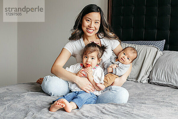 Asiatische chinesische glückliche Mutter sitzt mit Tochter und neugeborenem Sohn auf dem Bett.
