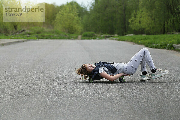 Das Kind liegt auf einem Skateboard.