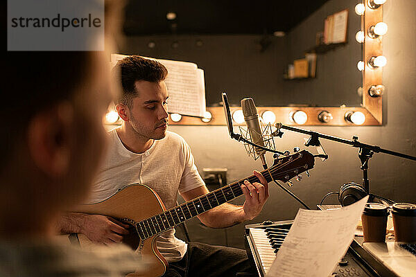 Männlicher Musiker spielt Gitarre in der Nähe des Songschreibers  während er im Studio Musik macht