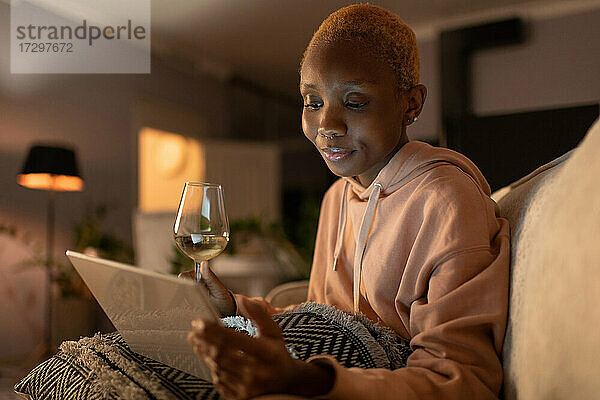 Schwarze Frau mit Wein und Tablette ruht sich zu Hause aus