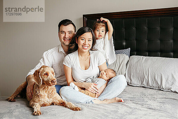 Glückliche gemischtrassige Familie mit Kindern und Hund auf dem Bett zu Hause