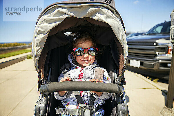 Lächelndes Mädchen mit Sonnenbrille  das im Kinderwagen sitzt