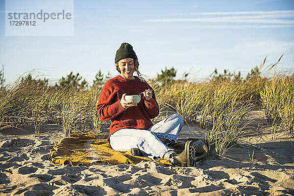 Junge Frau  die eine Suppe genießt  während sie allein im Auto am Strand campiert