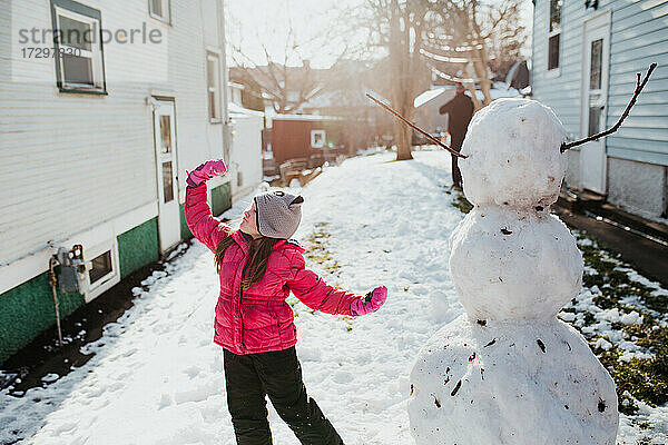 junges Mädchen posiert mit ihrem Schneemann nach einem Frühlingsschneefall