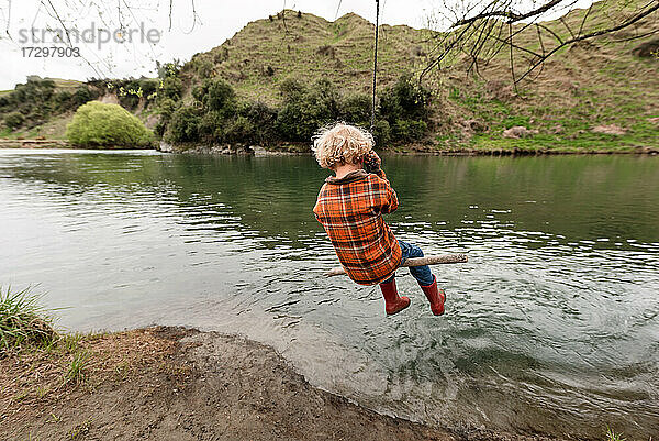 Kleines lockig behaartes Kind schaukelt am Fluss