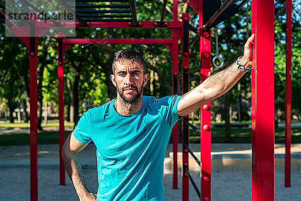 Porträt einer brünetten spanischen Sportlerin nach dem Training. Rote Calisthenics Bars im Hintergrund. Outdoor-Fitness-Konzept.