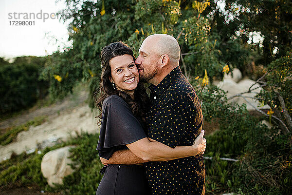 Ehemann umarmt & küsst Ehefrau im Garten in San Diego