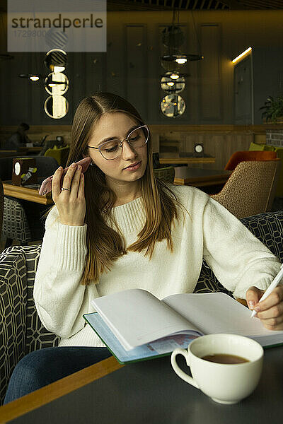 Frau mit Brille hört sich die Audiobotschaft an und schreibt eine Notiz im Café