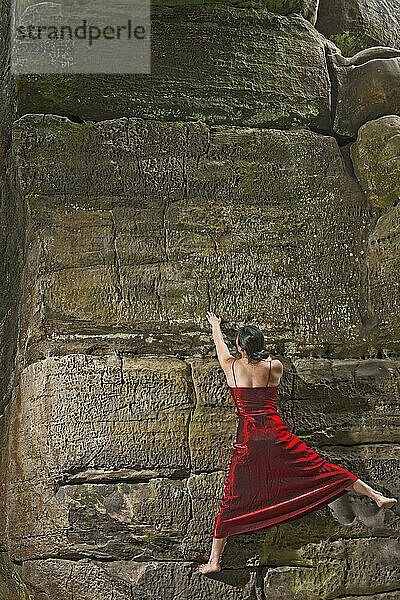 Frau in rotem Kleid beim Bouldern an den Sandsteinfelsen