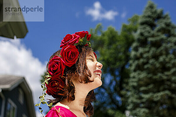 Ein schönes Mädchen mit einer Rosenkrone lächelt unter einem blauen Himmel