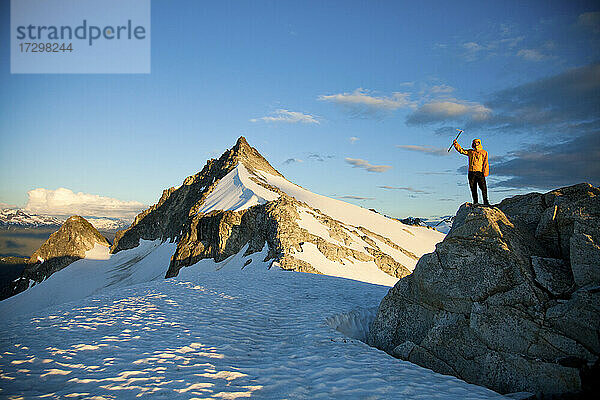 Erfolgreicher Kletterer mit gelber Jacke steht auf einem Felsvorsprung.