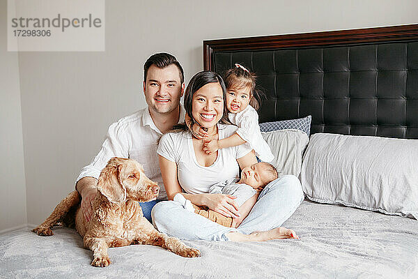 Glückliche multirassische junge Familie mit Kindern und Hund auf dem Bett.