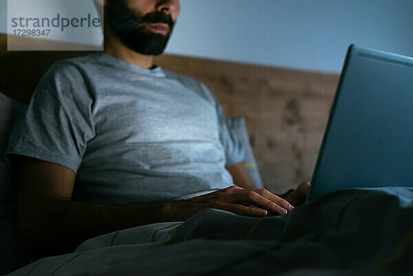 Crop Mann mit einem Laptop auf dem Bett in der Nacht