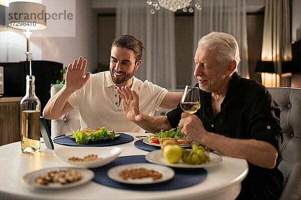 Junge und ältere Männer beim Videoanruf während des Abendessens