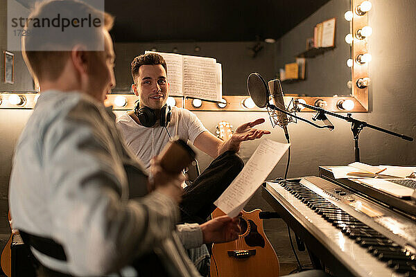 Erwachsene Männer lächeln und sprechen über Songtexte  während sie im Studio Musik machen